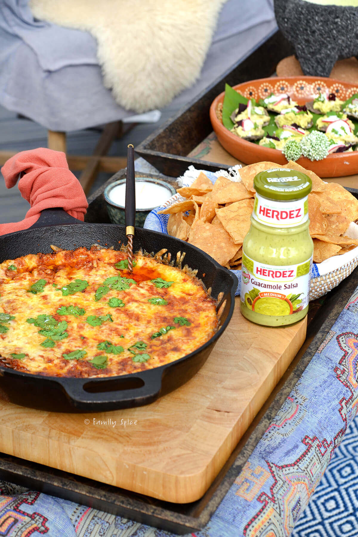 A large cast iron skillet with chorizo cheese dip, tortilla chips and a bottle of guacamole salsa next to it