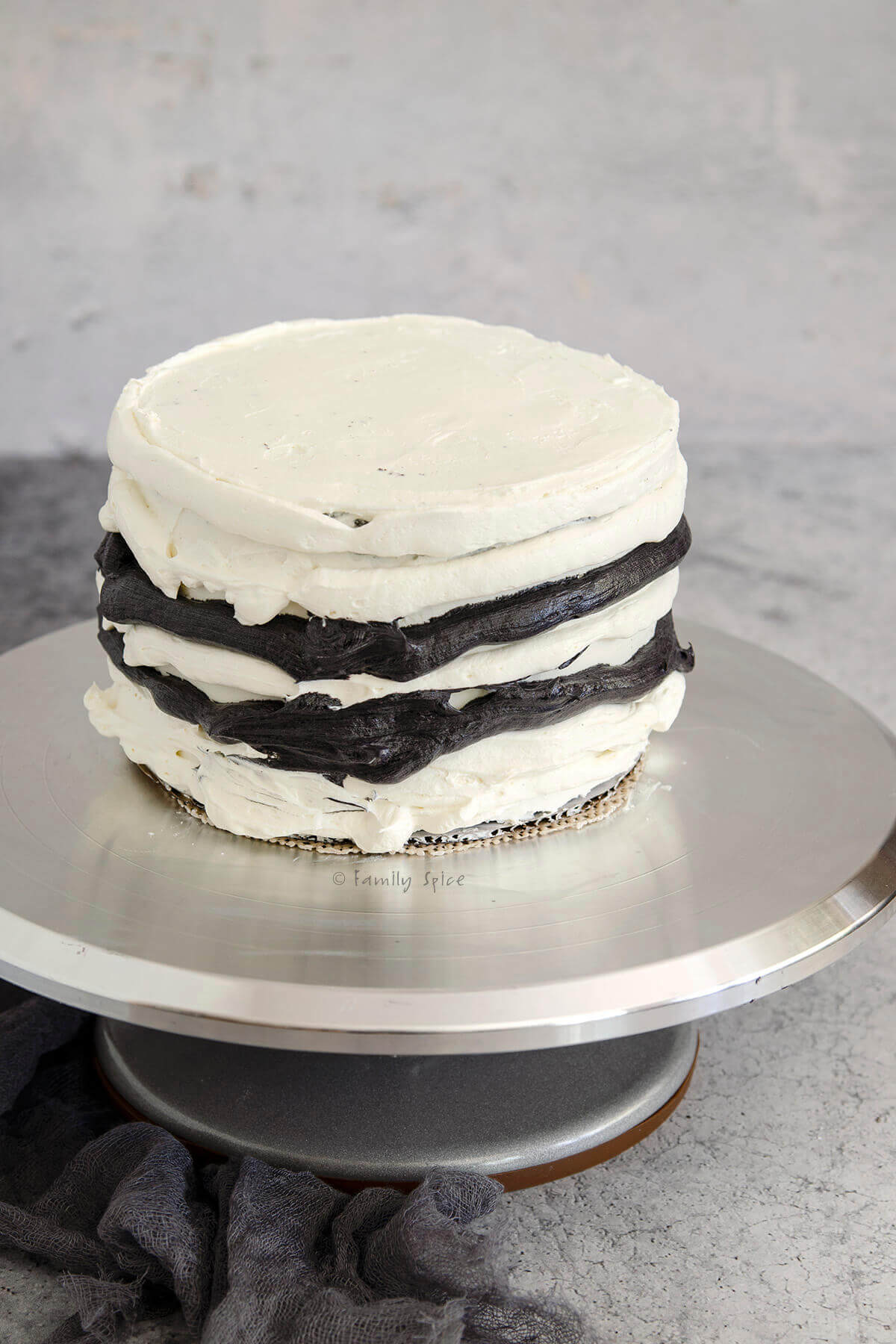 A 3-layer 6-inch cake with white and black frosting piped on it on a stainless cake stand