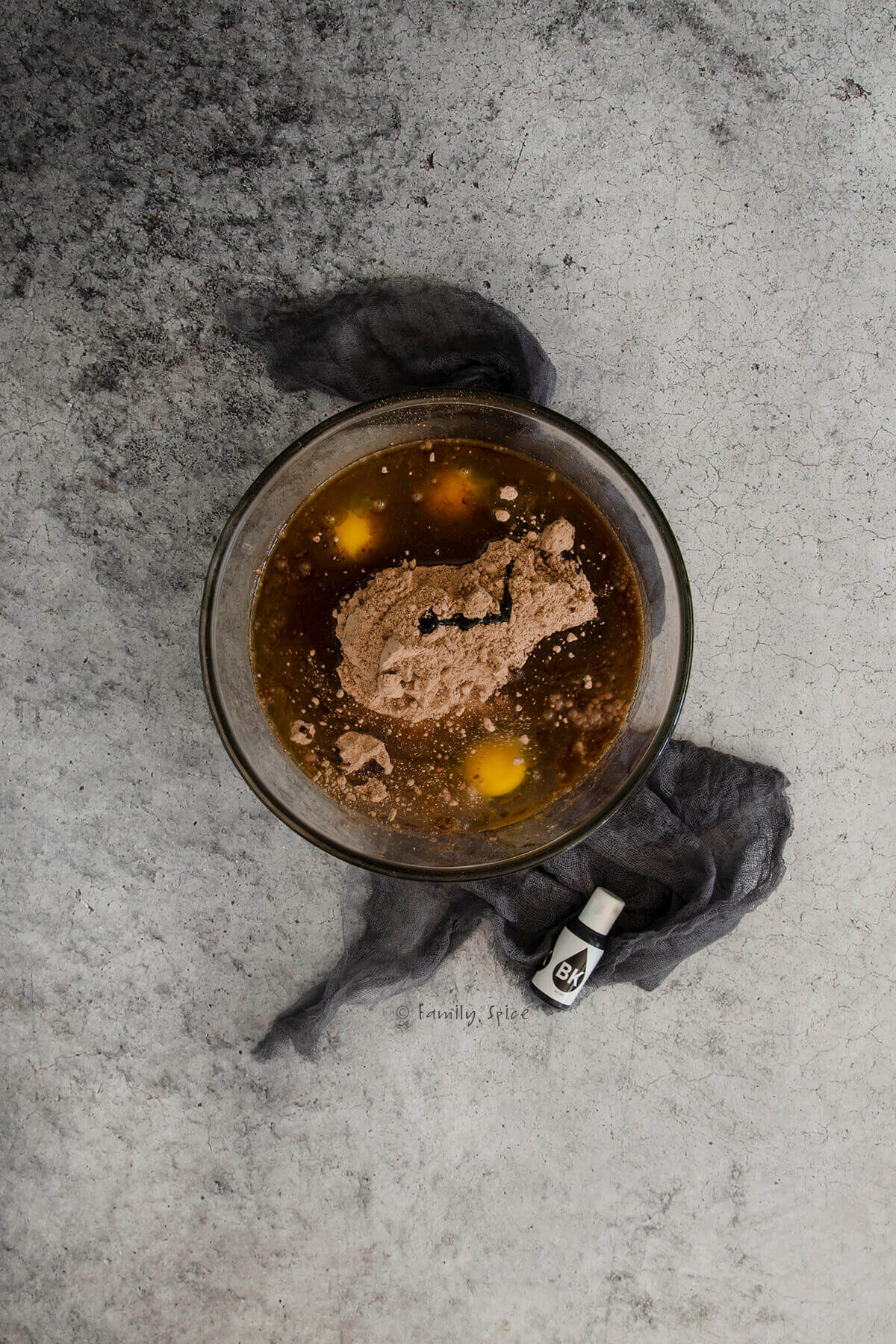A glass mixing bowl with chocolate cake mix, eggs, oil, water and black food coloring in it