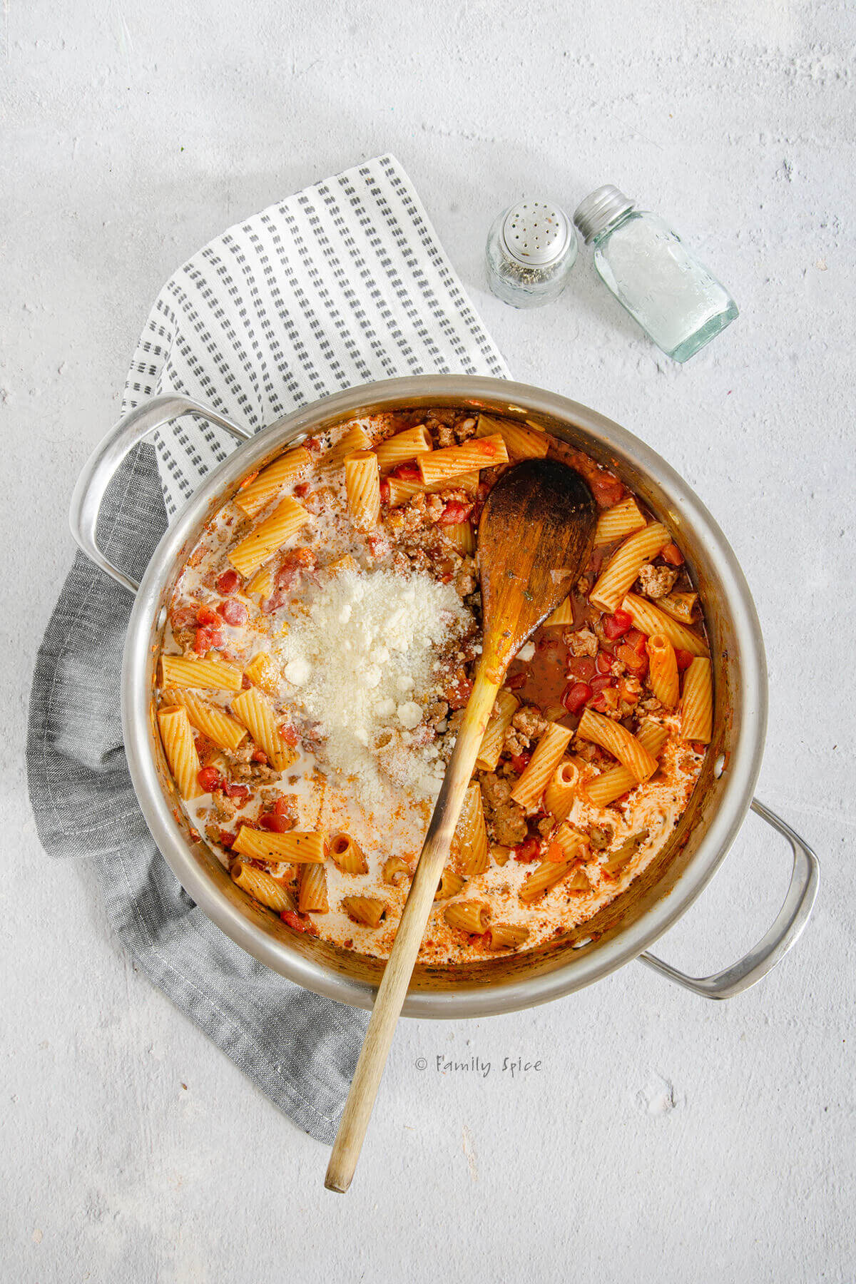 Grated parmesan and cream added to bolognese sauce with partially cooked rigatoni in a stainless pot