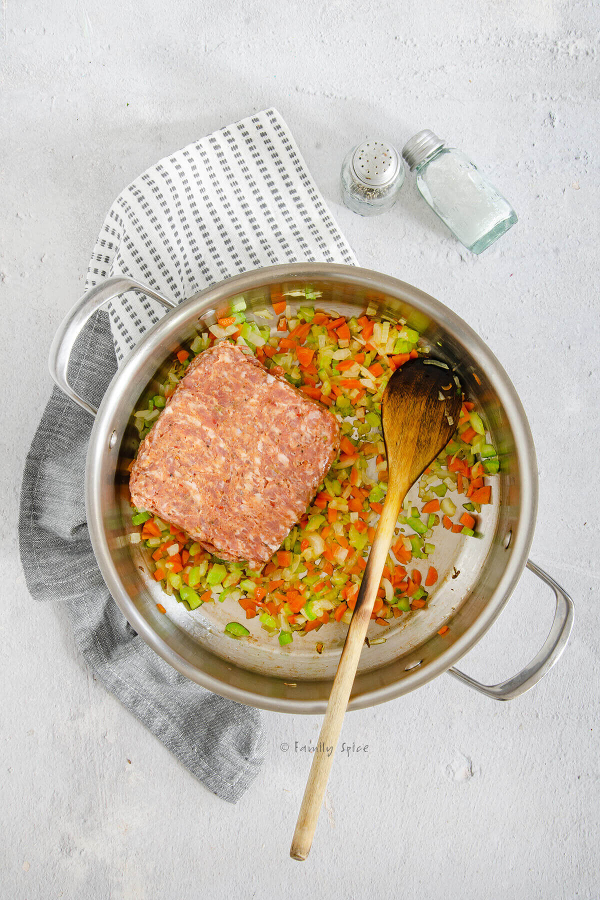 A brick of ground sausage added to vegetable mixture in a stainless pot