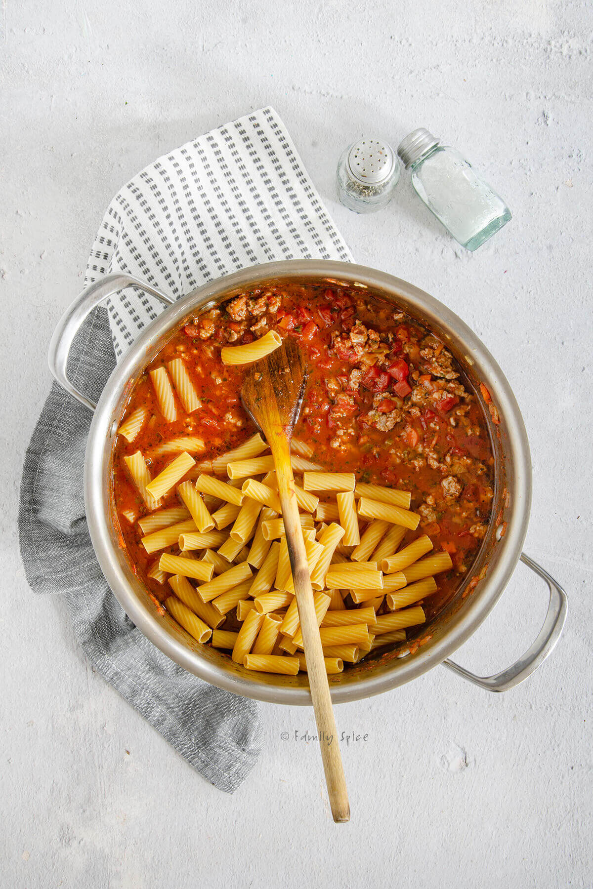 Rigatoni pasta added to bolognese sauce in a stainless pot