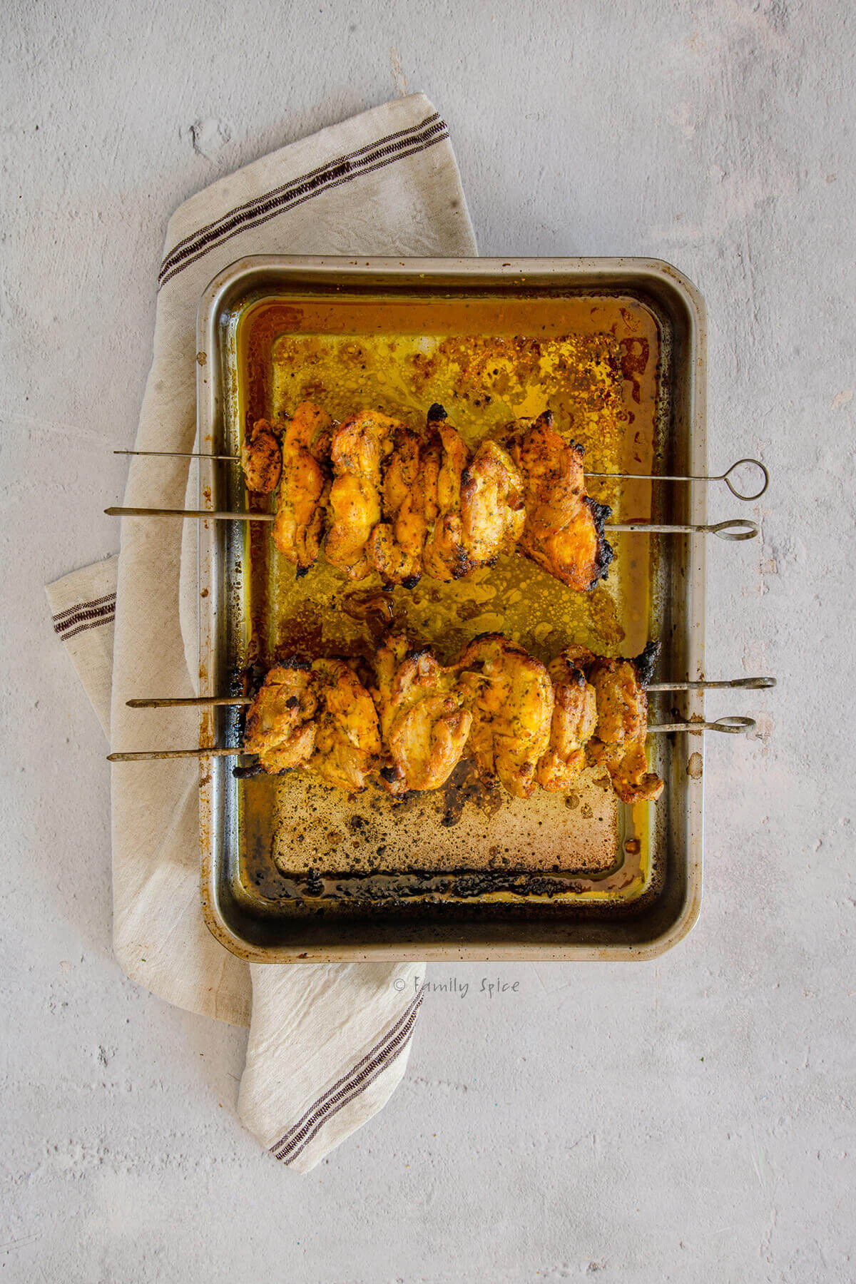 Two skewers of cooked chicken kebabs set over a roasting pan
