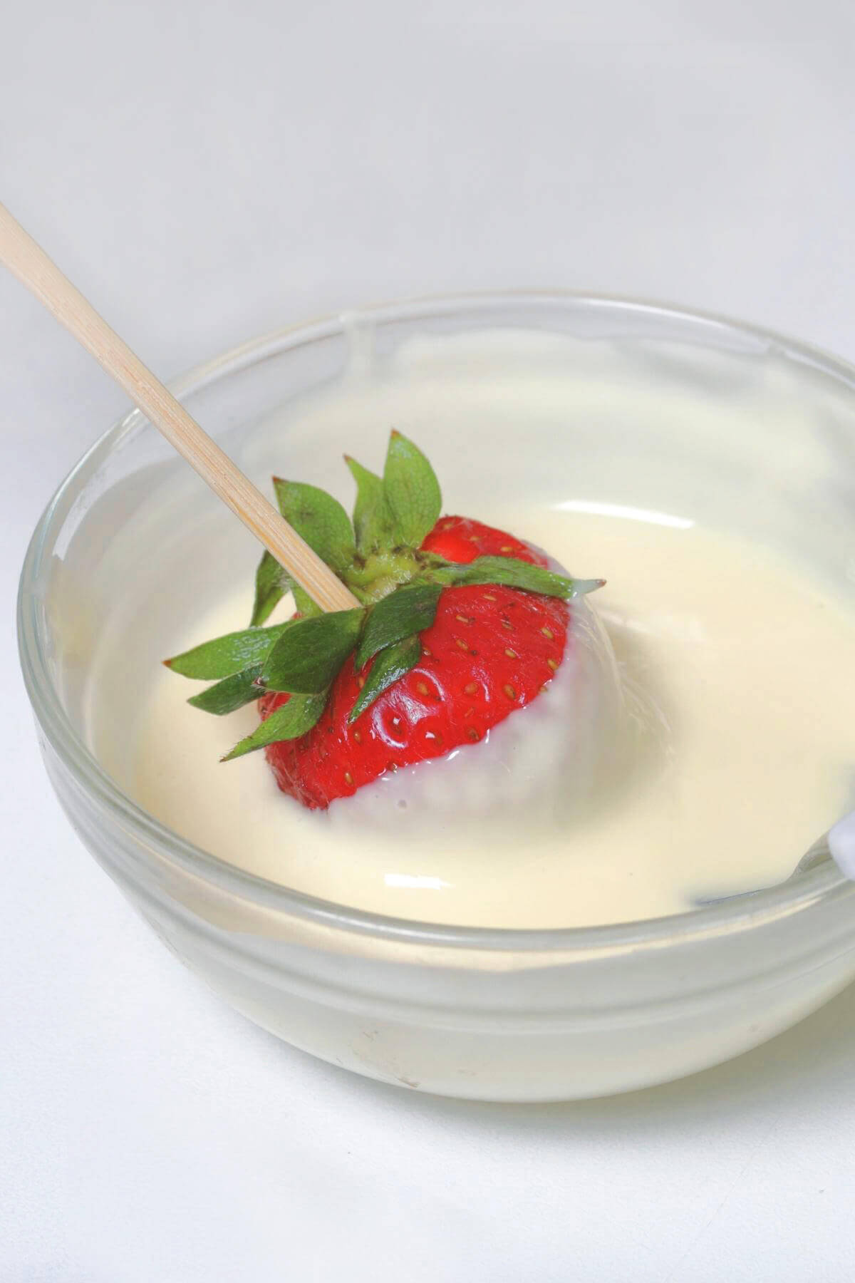 A strawberry with a skewer in it dipping into a small bowl of melted white chocolate