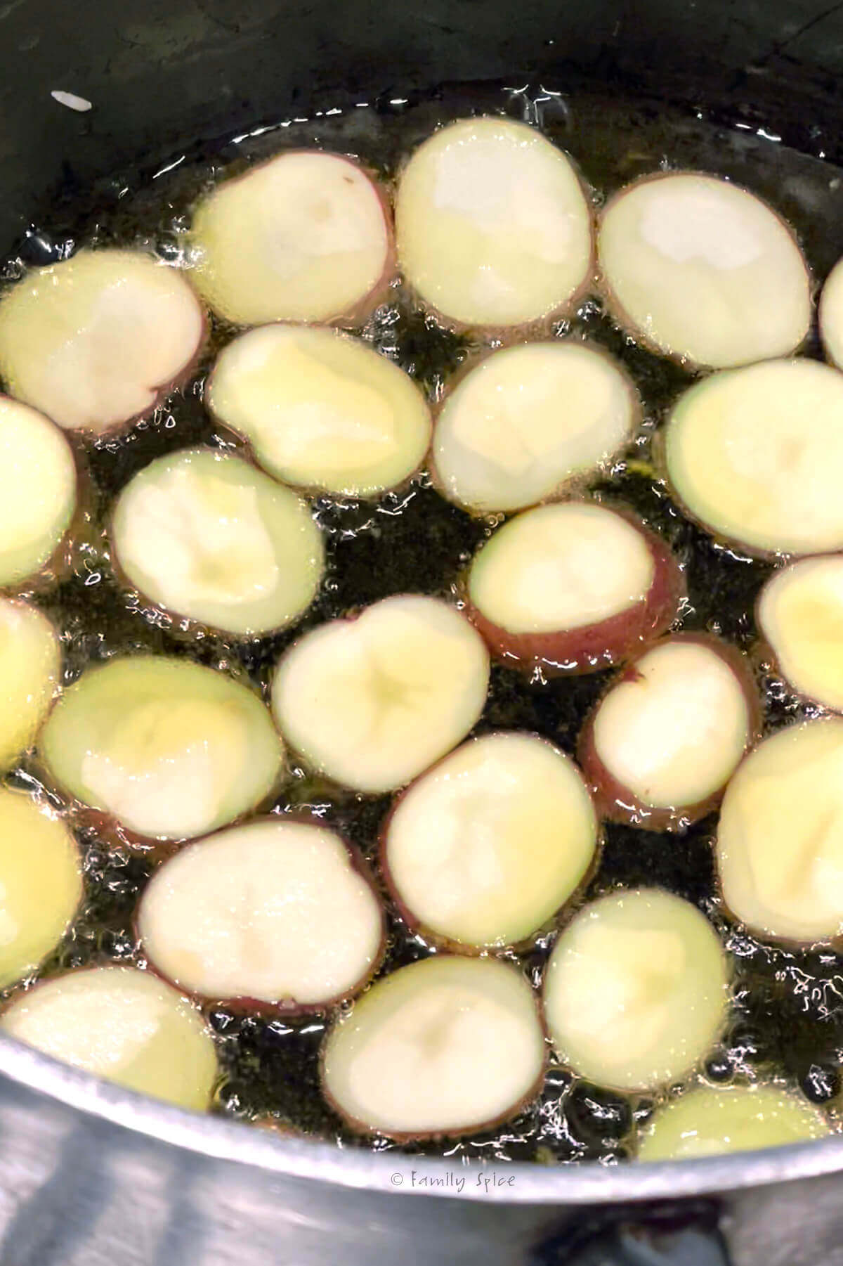 Bottom of a large nonstick pot with potato slices simmering in oil