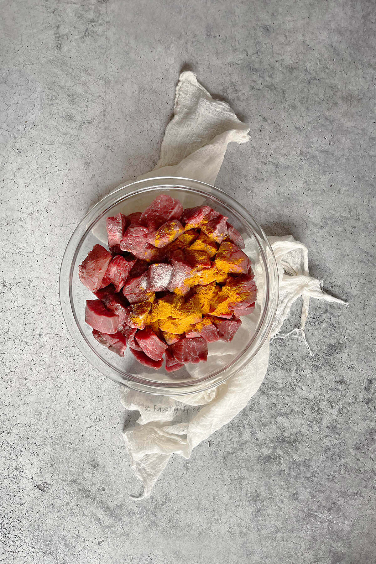 A glass mixing bowl with beef stew meat with salt, flour and turmeric