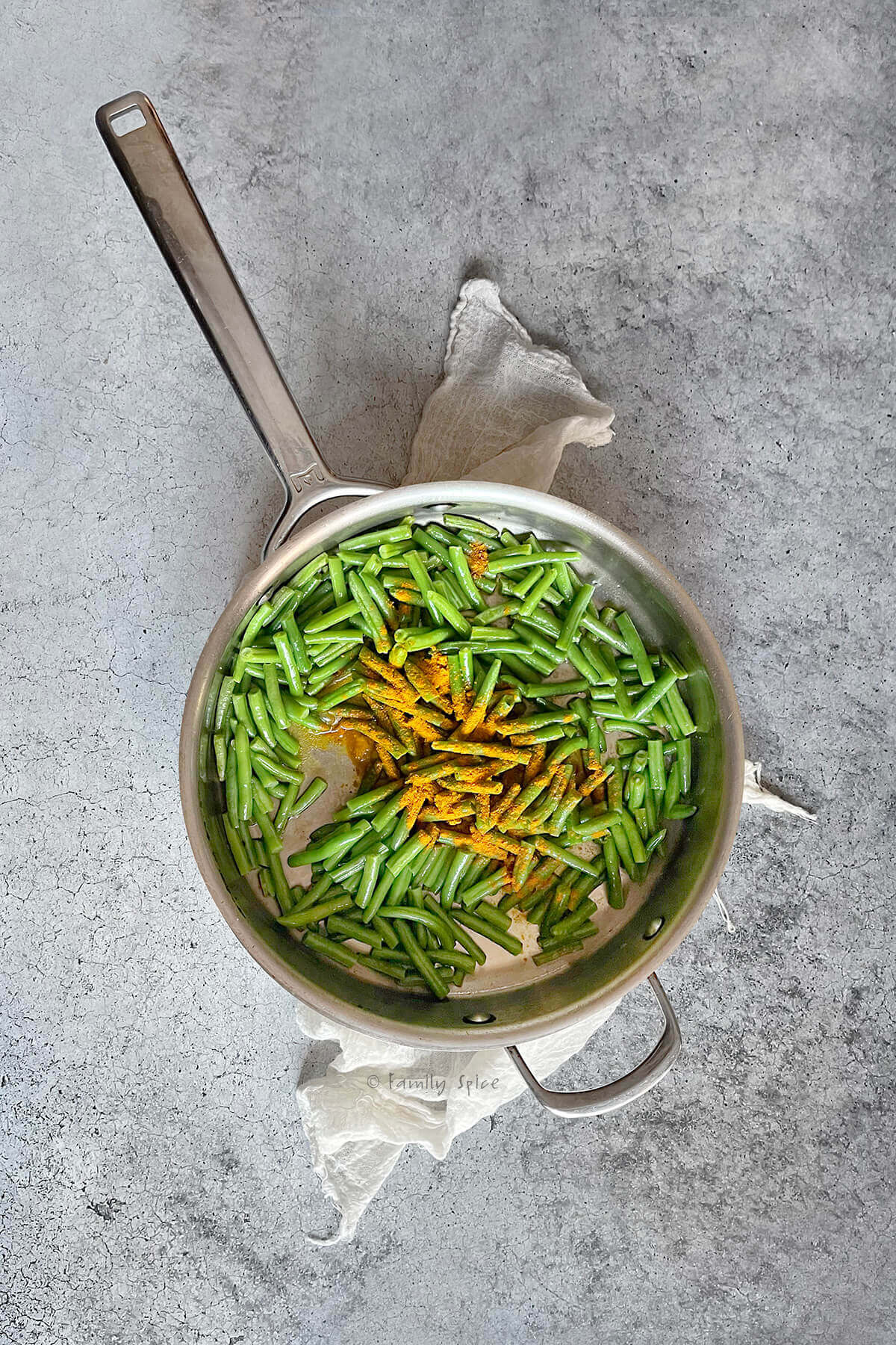 Top view of a stainless pan with cut green beans topped with turmeric in it