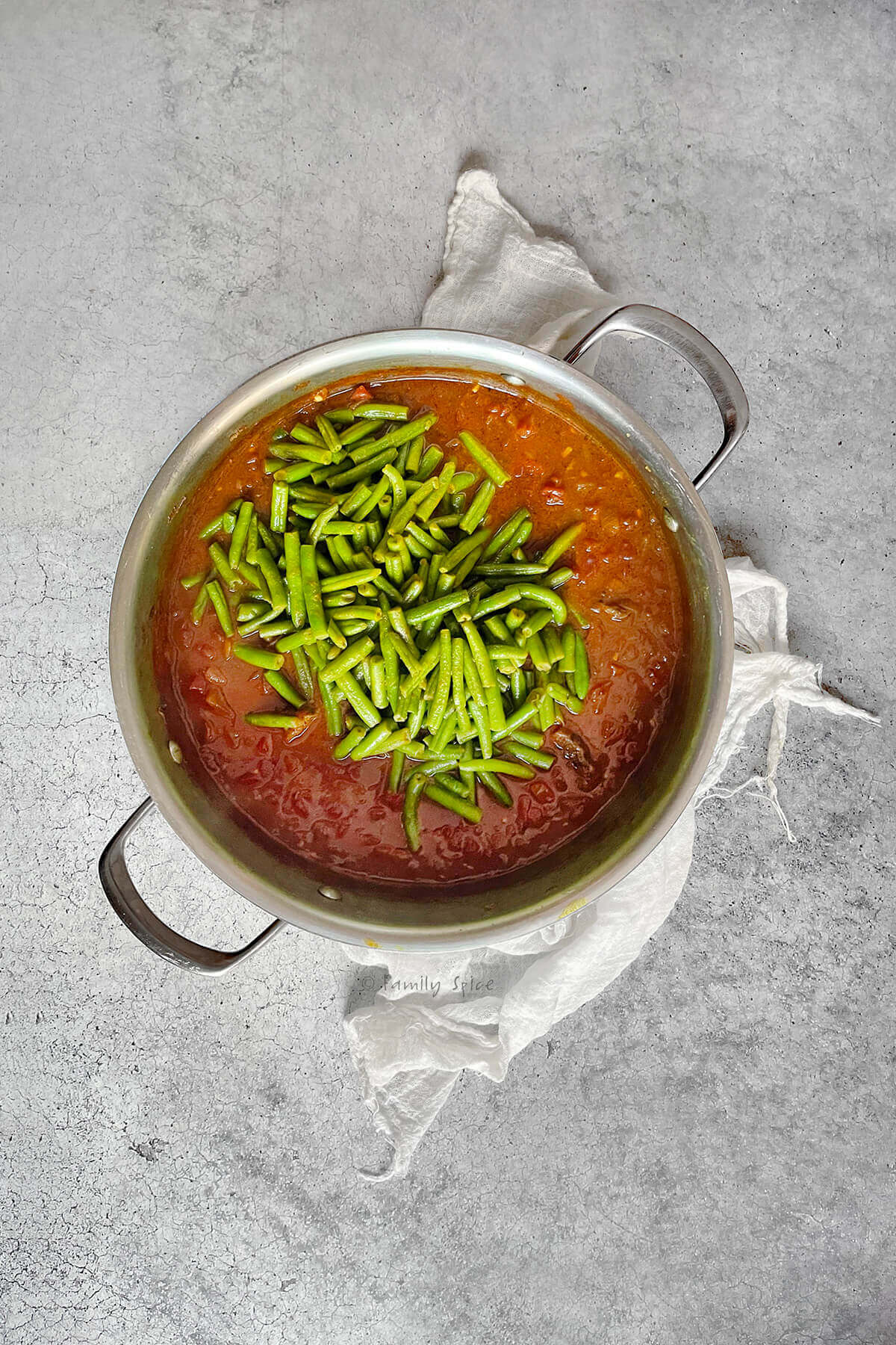 Adding chopped green beans to tomato-beef stew meat simmering in a stainless pot