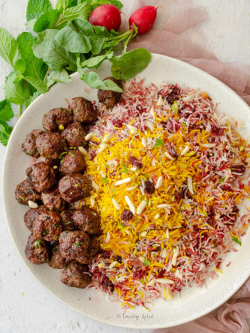 Closeup of top view of a round platter filled with albaloo polo (sour cherry rice) and lamb meatballs