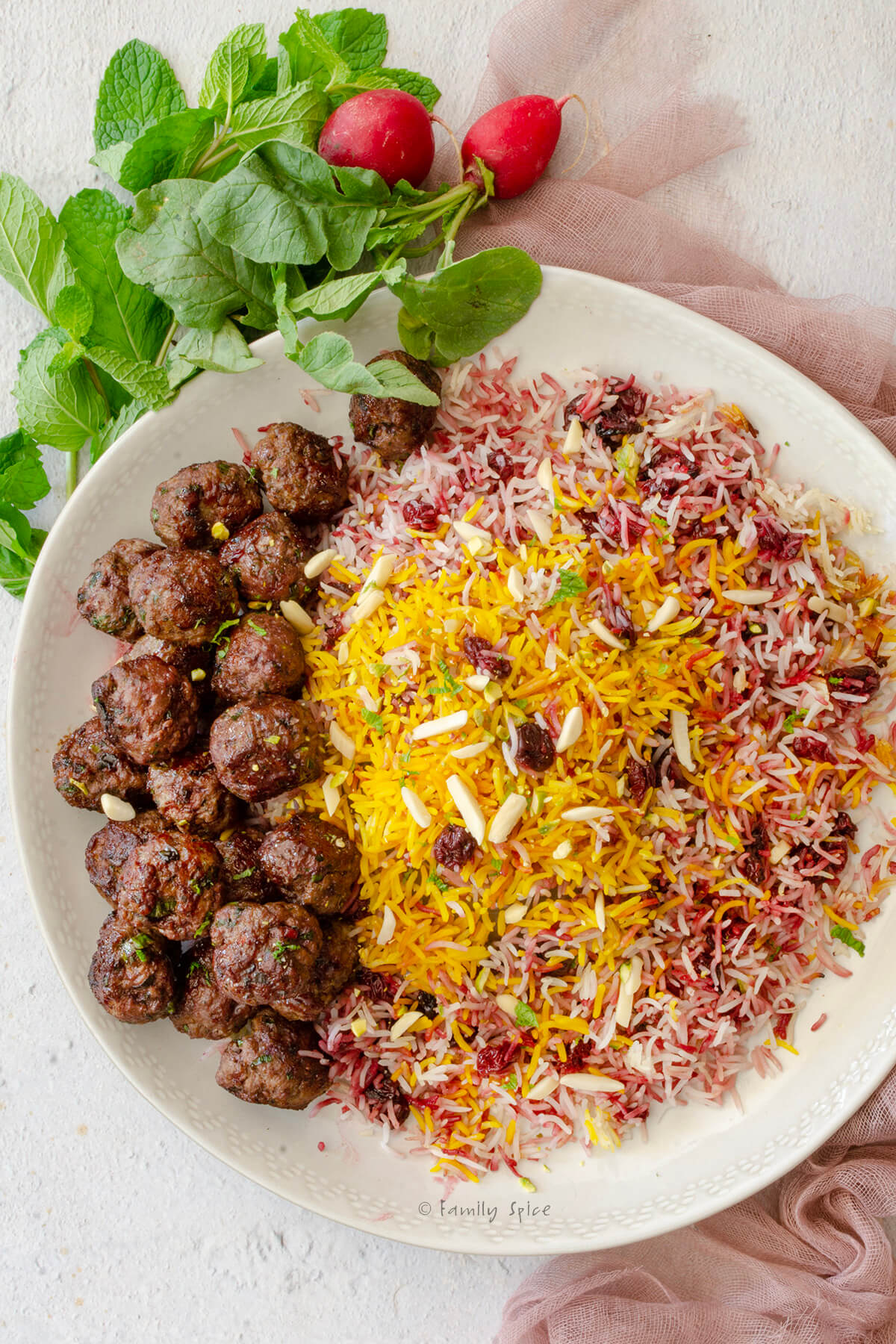 Closeup of top view of a round platter filled with albaloo polo (sour cherry rice) and lamb meatballs