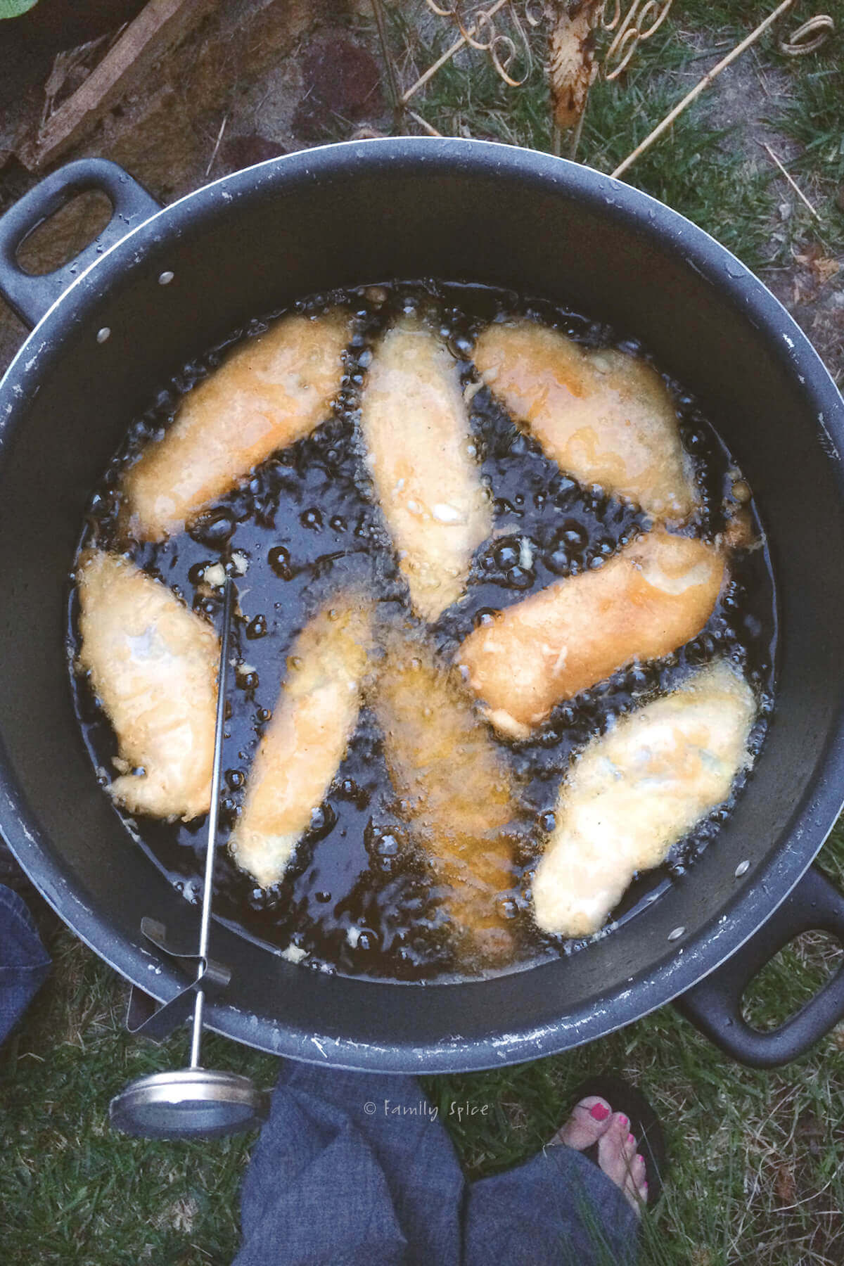 Top view of a large pot with hot oil, beer battered fish frying in it and a thermometer attached