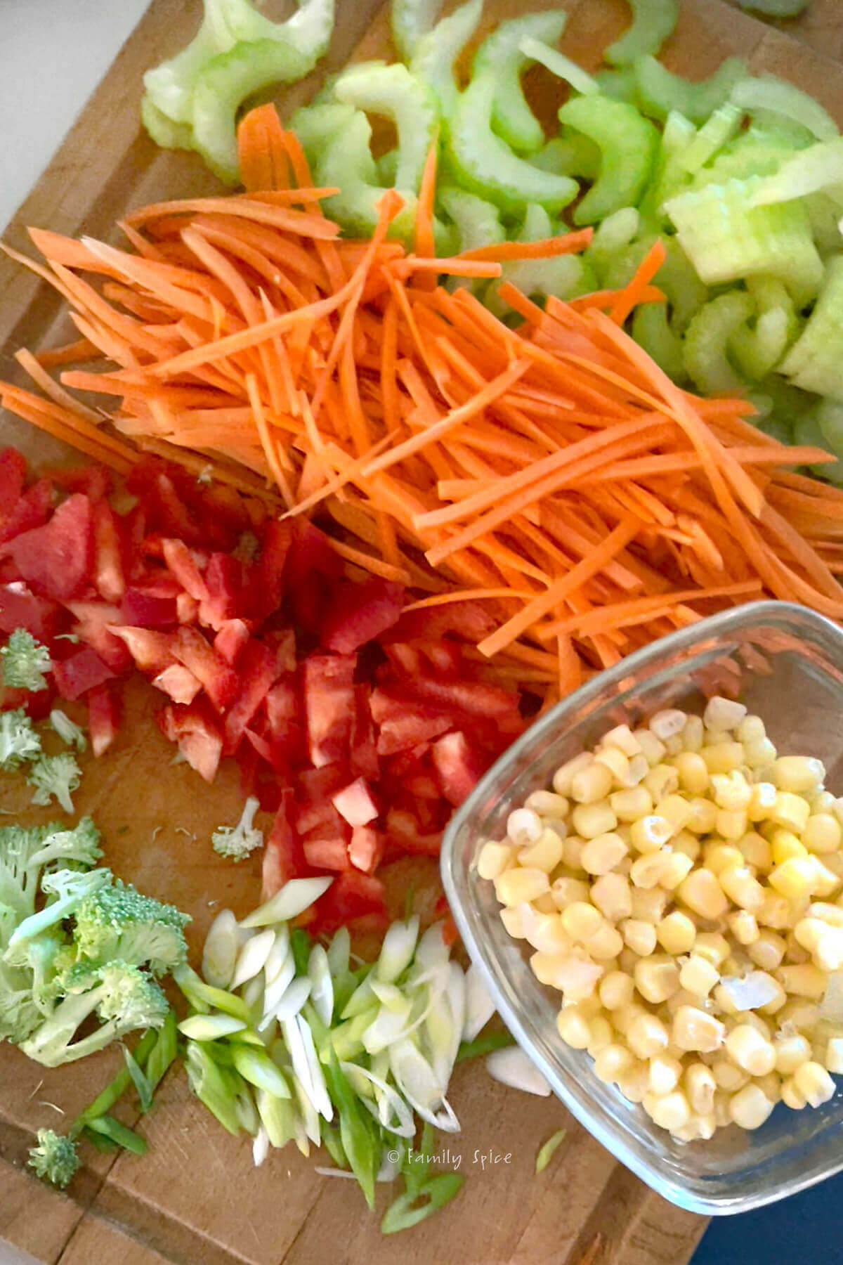 Chopped green onions, broccoli, red bell peppers, celery, carrots and corn on a chopping board