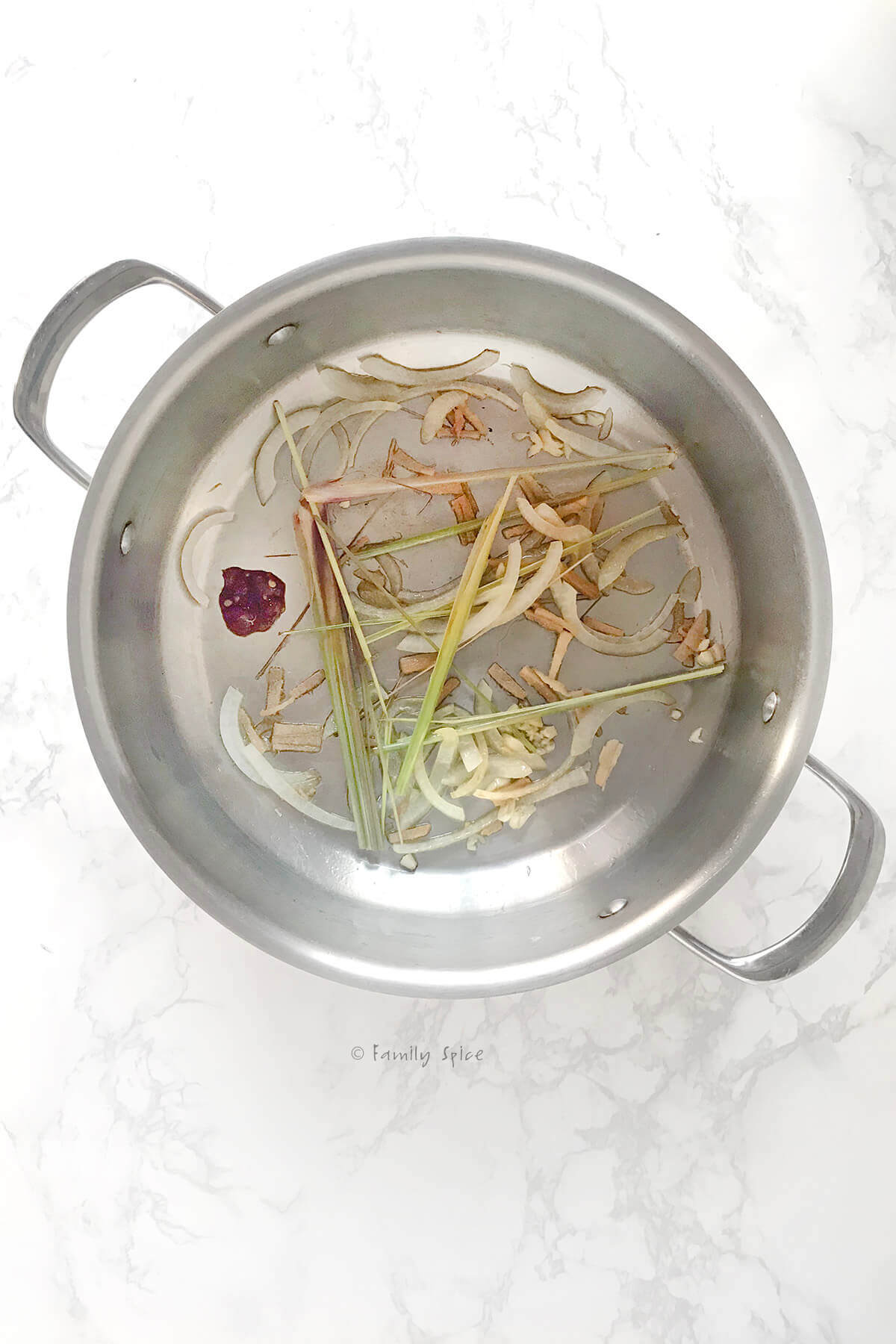 Top view of a stainless pot with sauteed onions, lemongrass, garlic and chile paste