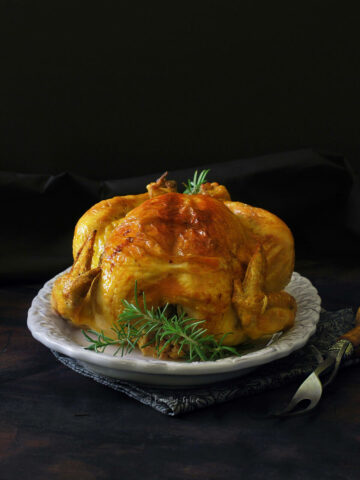 A roast chicken coated with saffron butter on a white dish with a dark table and background