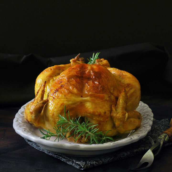 A roast chicken coated with saffron butter on a white dish with a dark table and background