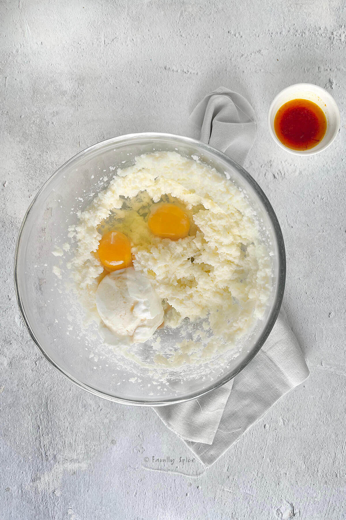 A mixing bowl with creamed butter and sugar with eggs and yogurt in it and a small bowl with saffron steeping