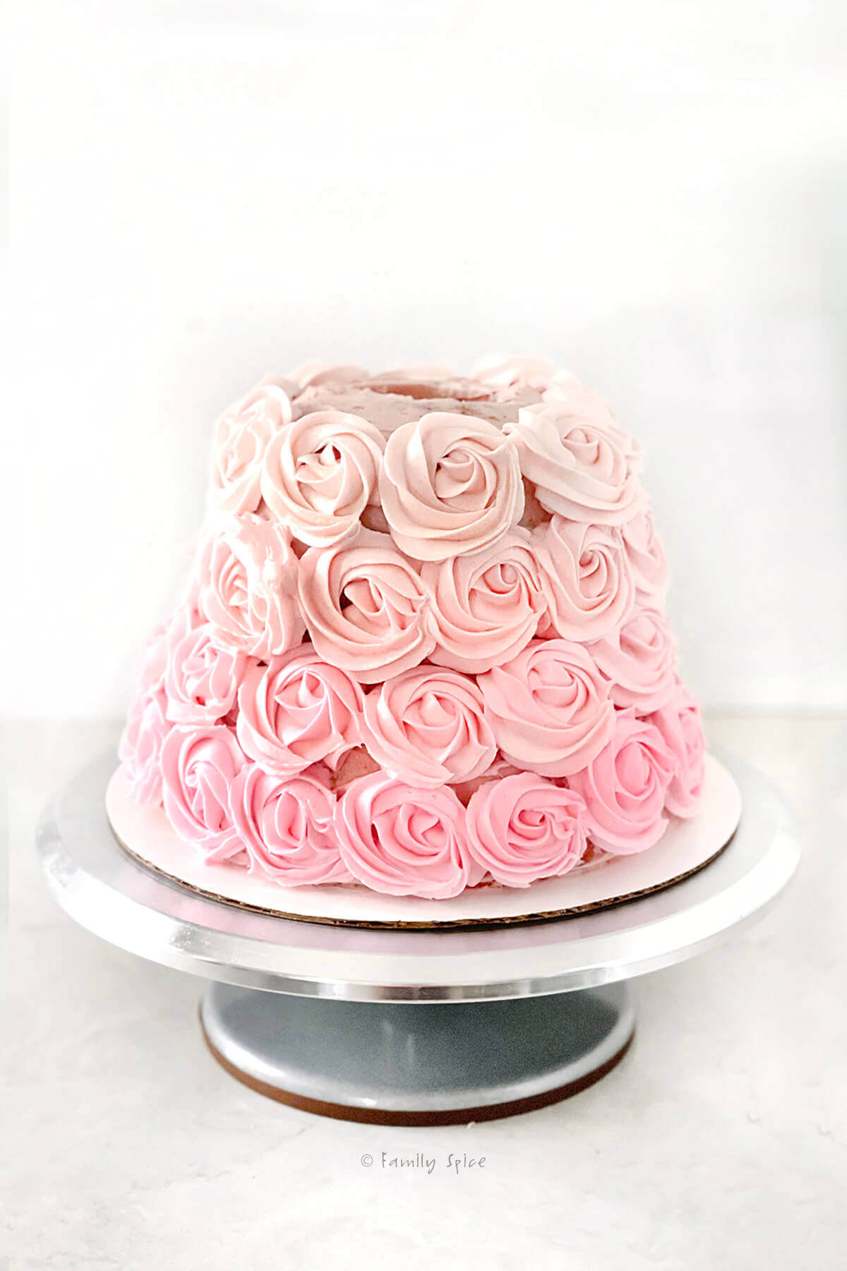 A bell shaped strawberry cake with ombre pink rosettes piped onto it
