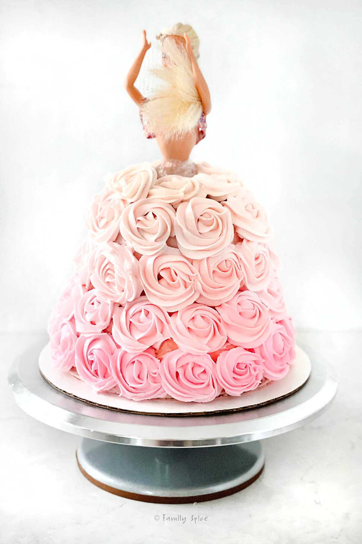 Adding pink ombre rosettes onto a barbie cake with a barbie inserted into it