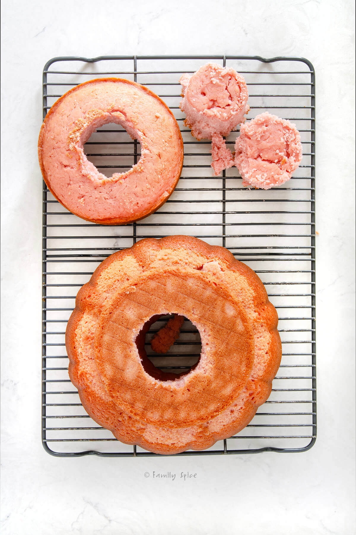 Top view of a pink strawberry bundt cake with a 6-inch strawberry cake with center cut out on top of it and another 6-inch inch cake with center cut out next to it on a cooling rack