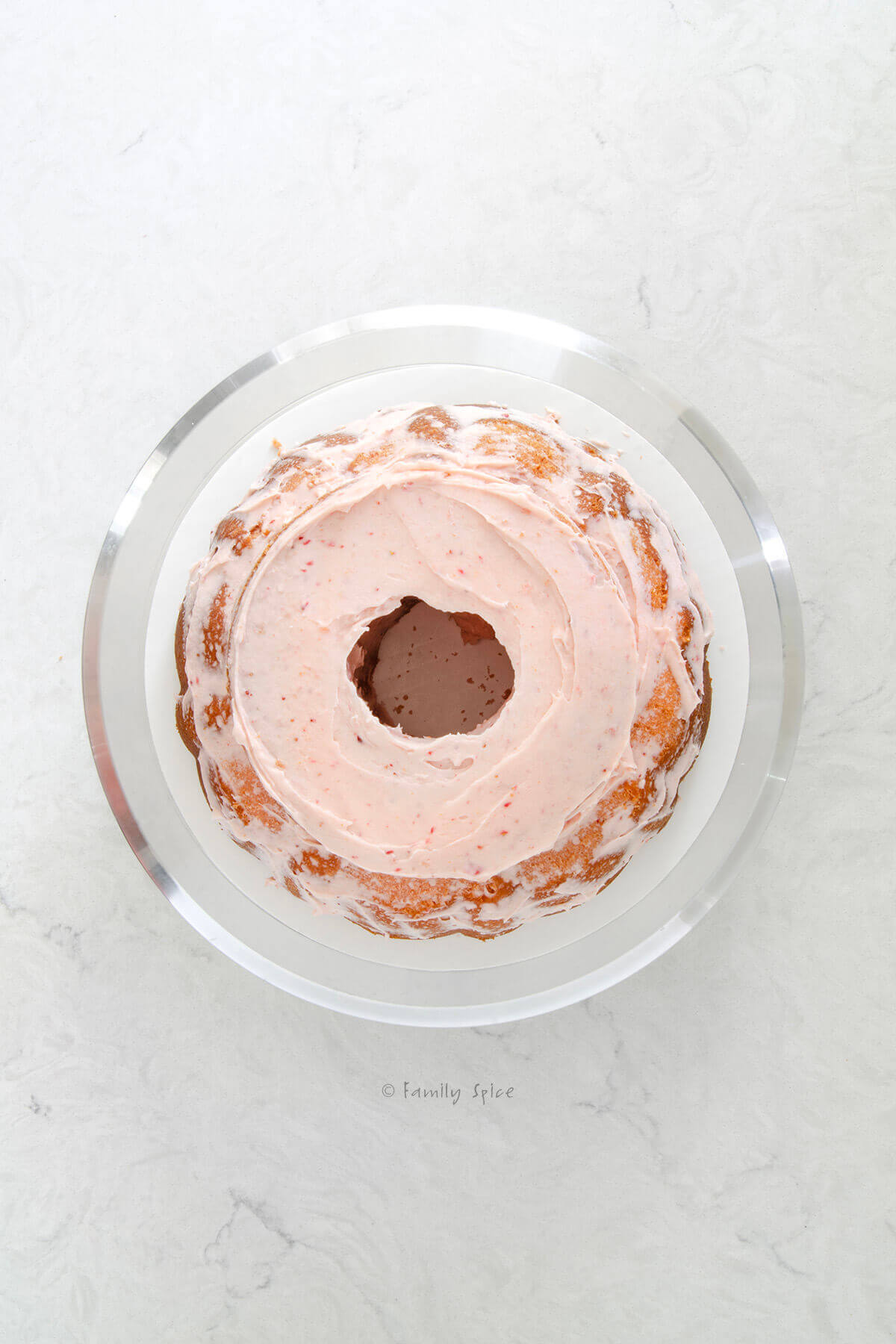 Top view of a pink frosted 6-inch strawberry cake added to a strawberry bundt cake on a cake stand with the center cut out