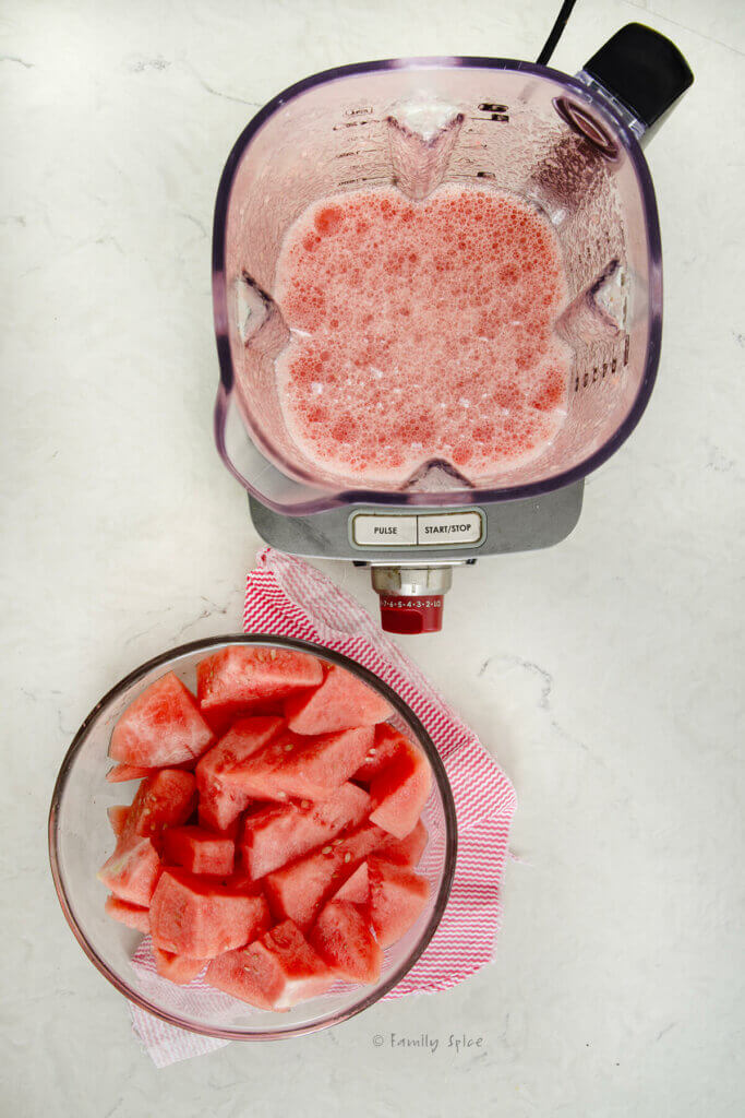 A bowl with cut up pieces of watermelon next to a blender filled with watermelon juice