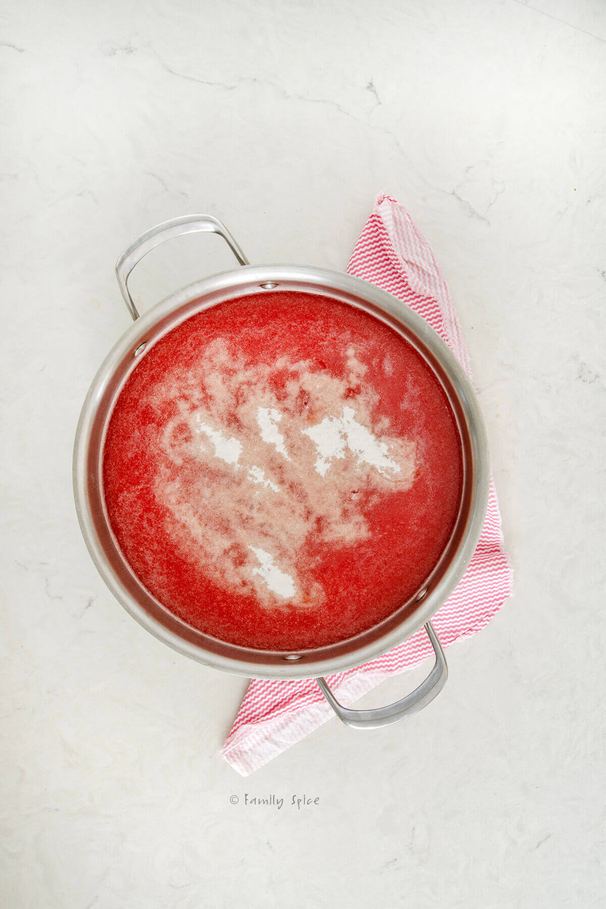 Top view of a stainless pot filled with strained watermelon juice and sugar