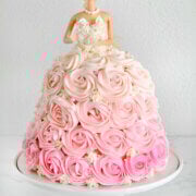 A barbie cake with pink ombre rosettes piped all over it with a white frosted corset sitting on a white cake stand