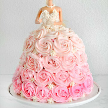 A barbie cake with pink ombre rosettes piped all over it with a white frosted corset sitting on a white cake stand