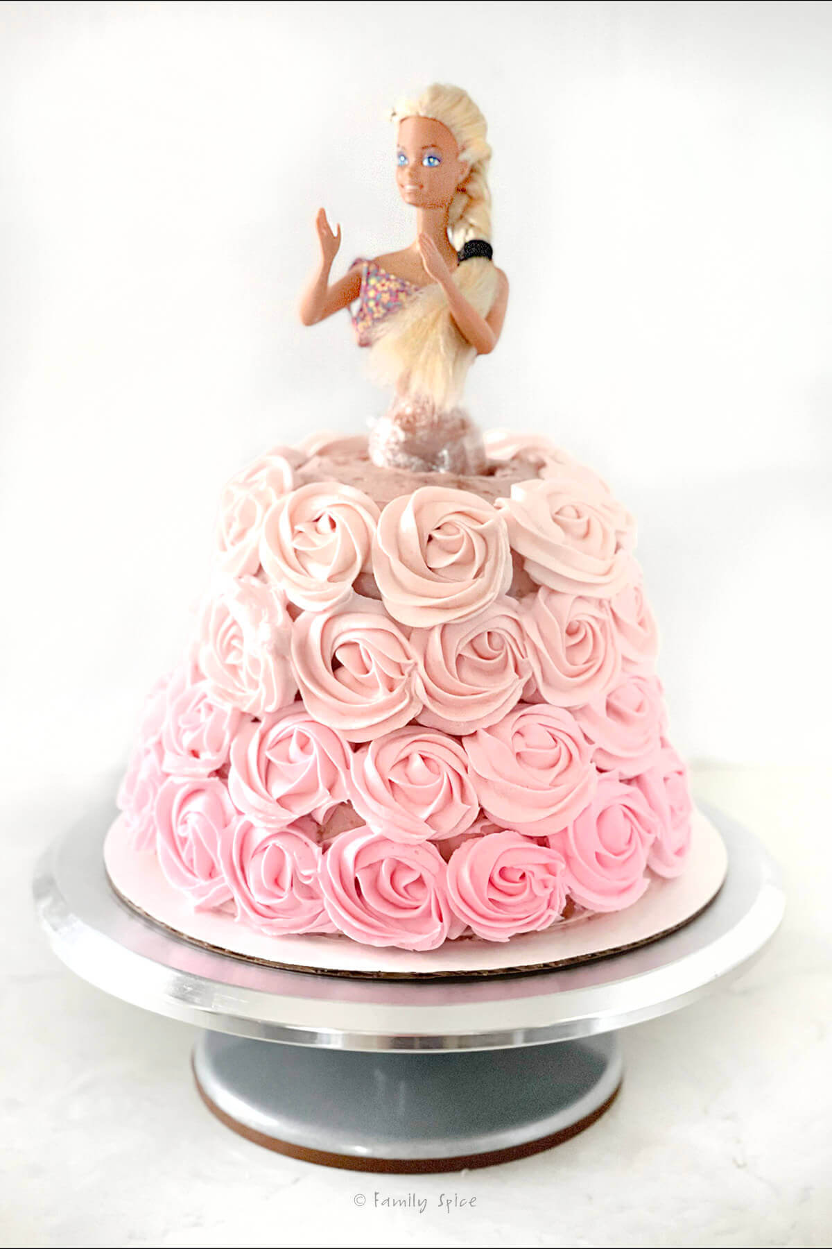 A classic barbie with legs wrapped in plastic wrap inserted into a strawberry cake with ombre pink rosettes
