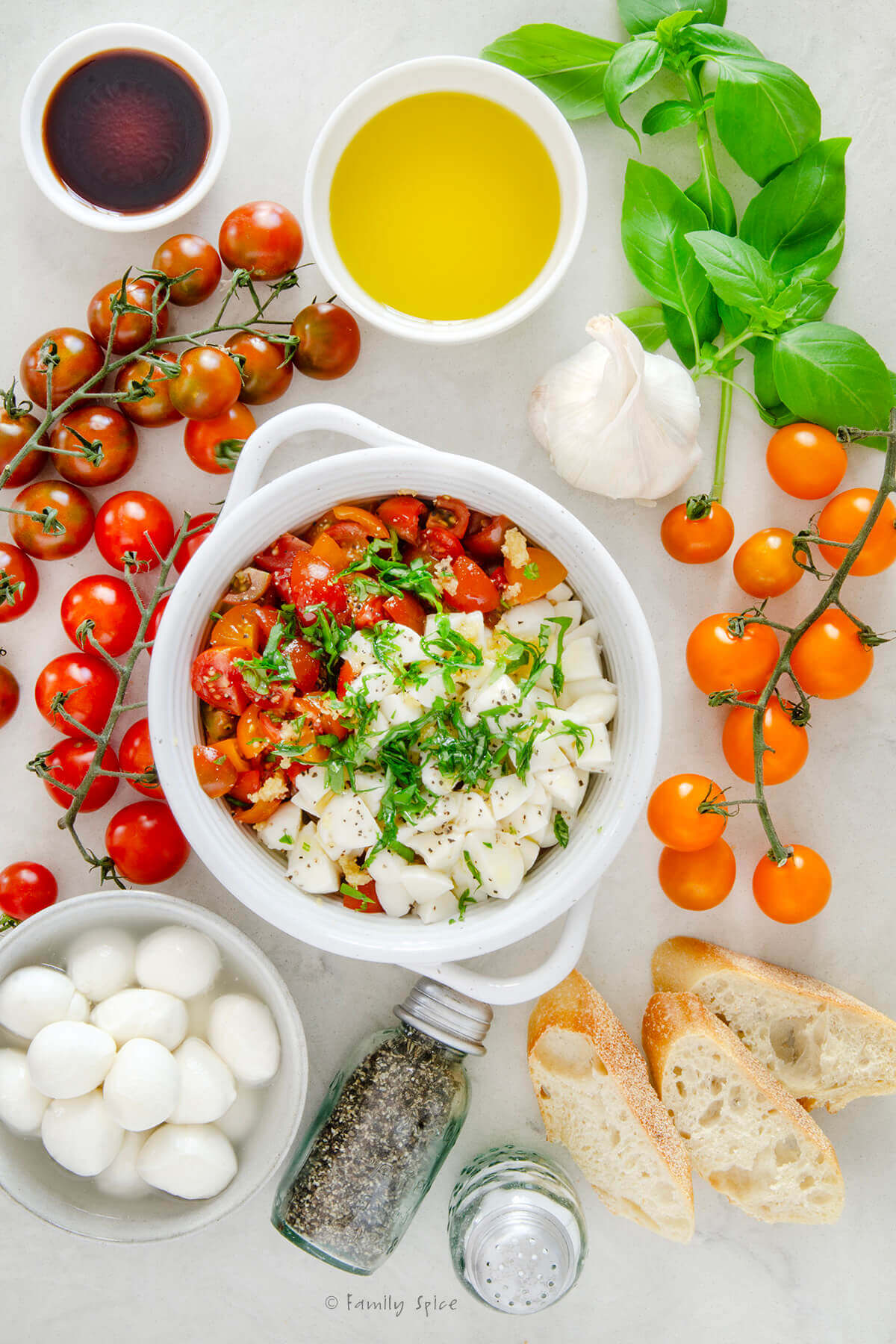 Top view of a bowl with chopped tomatoes, mozzarella, basil, oil and seasonings in it and fresh ingredients around it