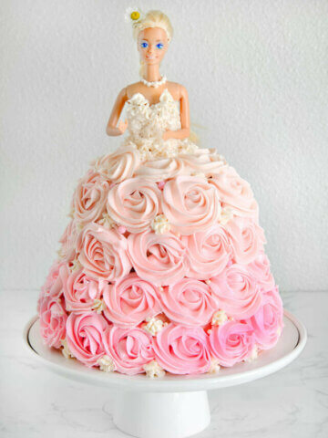 A barbie cake with pink ombre rosettes piped all over it with a white frosted corset sitting on a white cake stand
