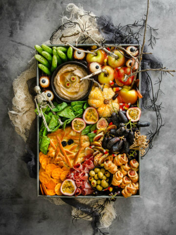 Top view of a spooky halloween charcuterie board on a dark background with various props