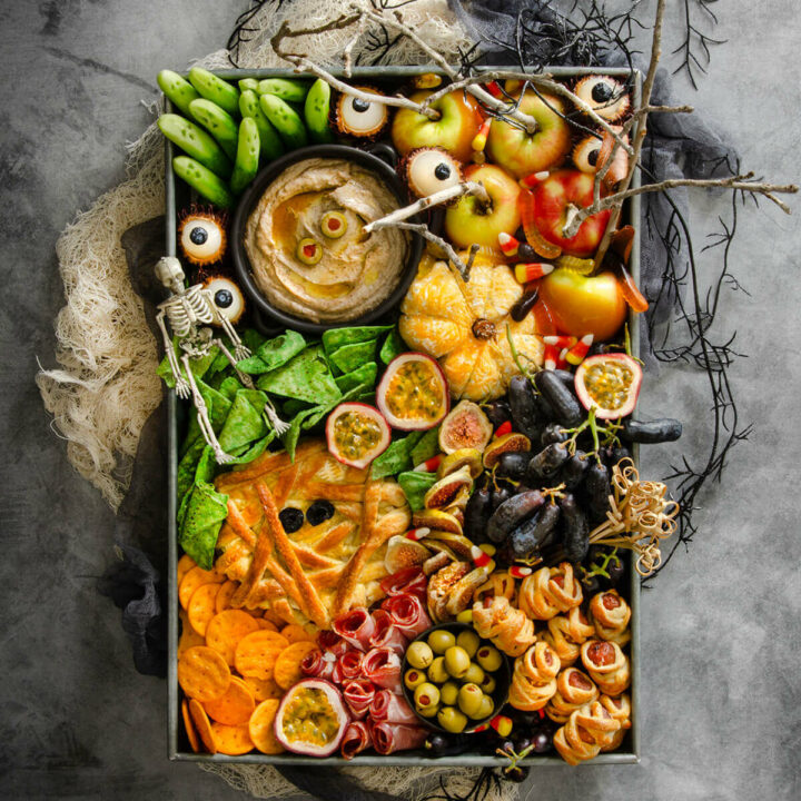 Top view of a spooky halloween charcuterie board on a dark background with various props