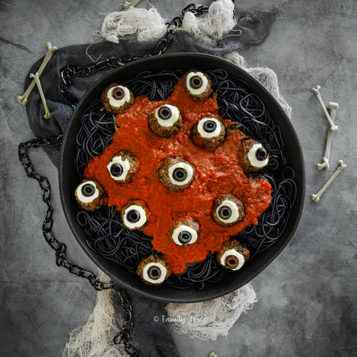 Top view of a black serving bowl with halloween pasta, black spaghetti, marinara and eyeball meatball