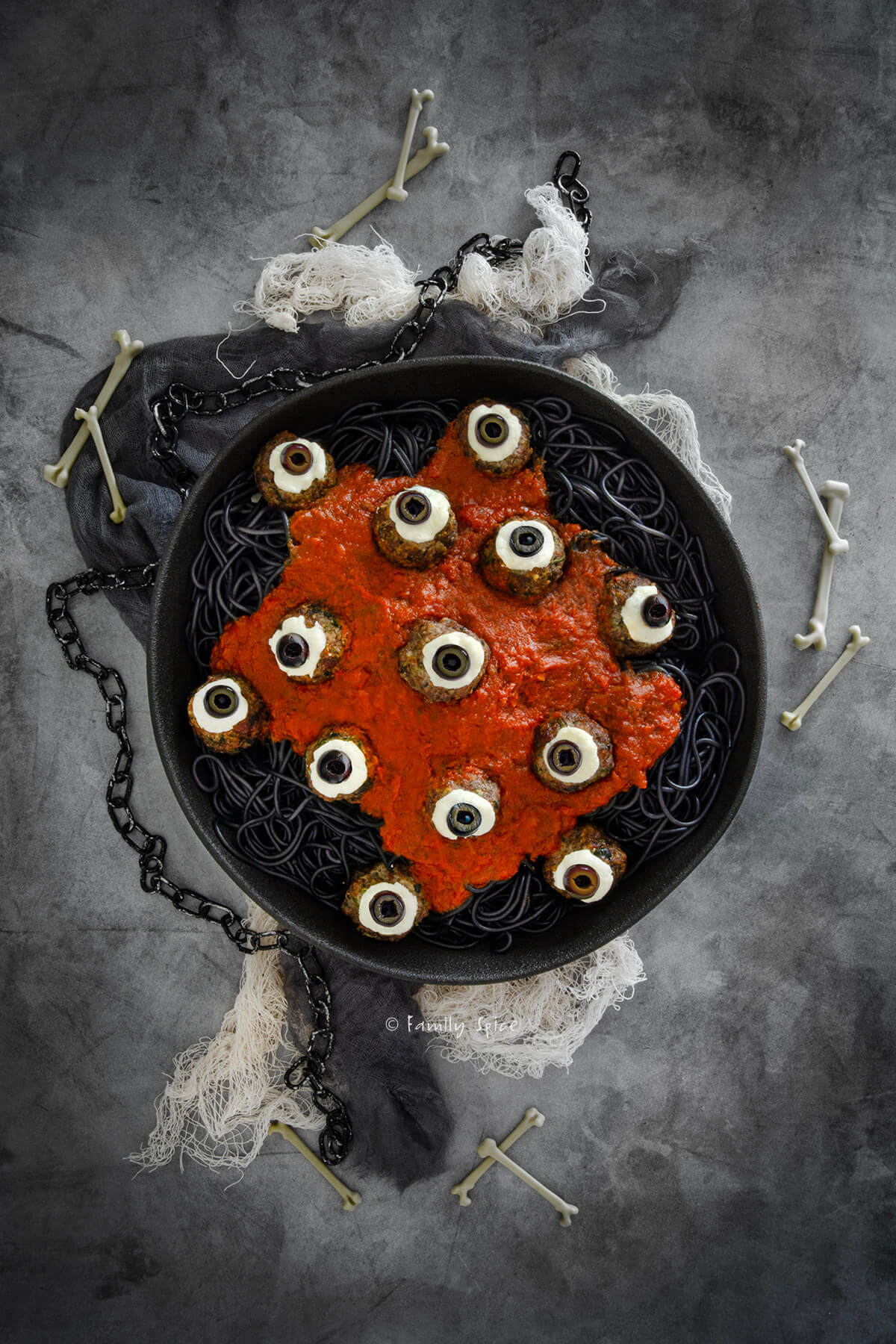 Top view of a black serving bowl with halloween pasta, black spaghetti, marinara and eyeball meatball