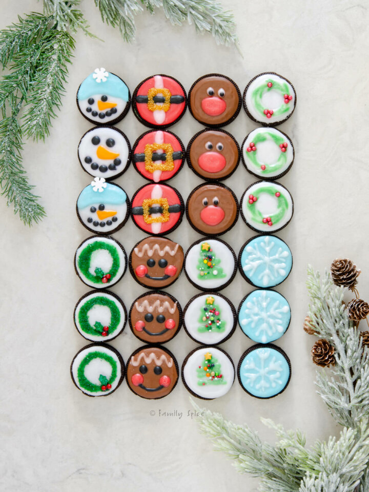 Top view of 8 different types of Christmas oreos: snowman, santa belt, reindeer, wreath, snowflake, christmas tree, gingerbread and another christmas wreath.