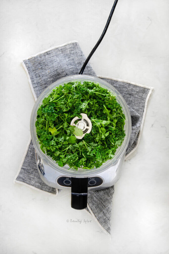 Top view of a food processor with fresh cilantro and parsley in it