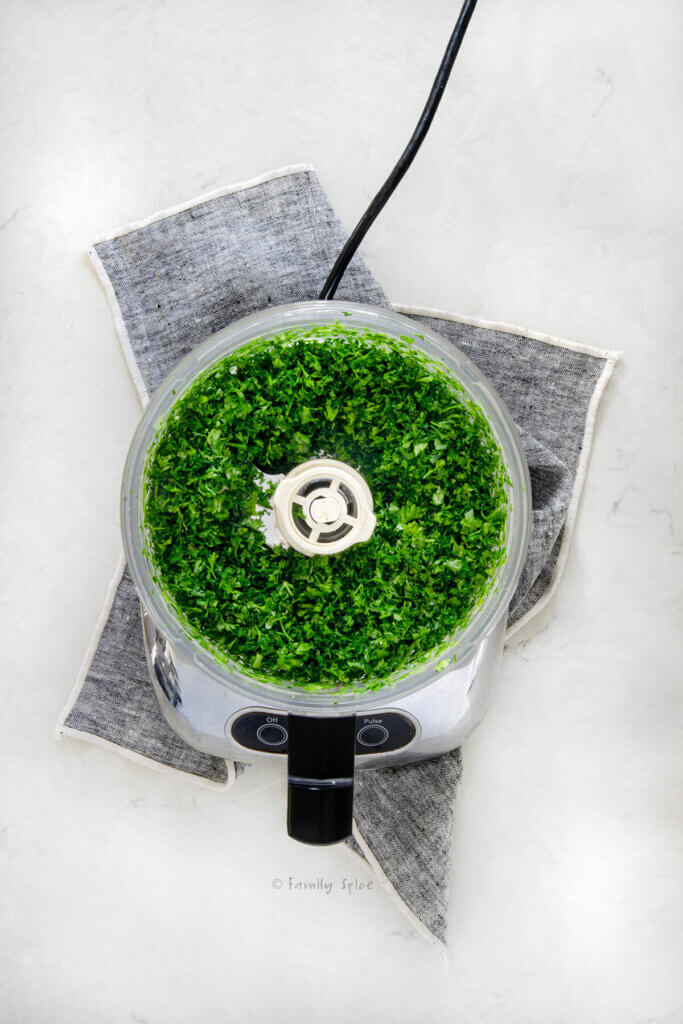 Top view of a food processor with chopped fresh cilantro and parsley in it