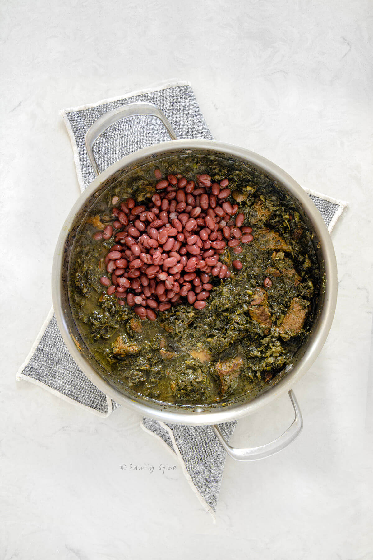 Top view of a stainless pot with ghormeh sabzi with small kidney beans added to it