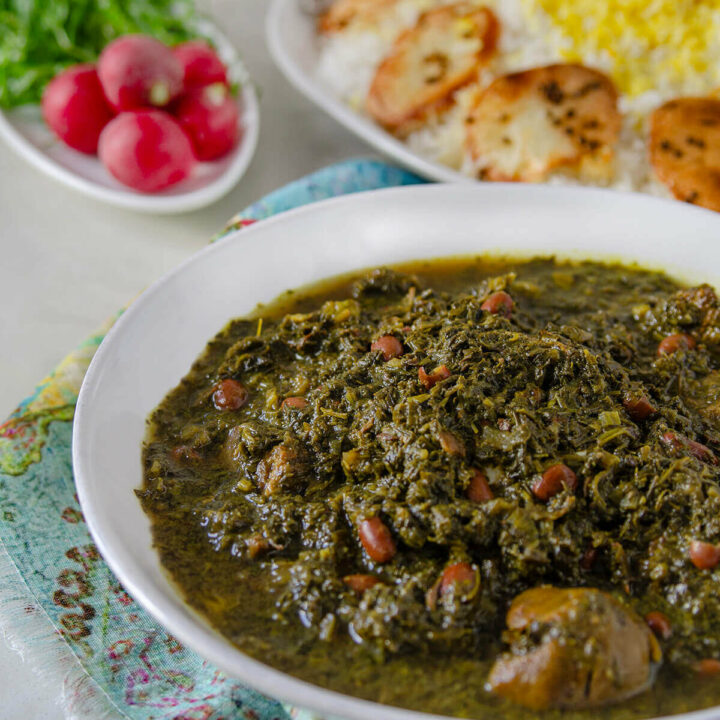 Side view of a bowl of ghormeh sabzi with Persian rice on a platter and fresh radishes and herbs behind it