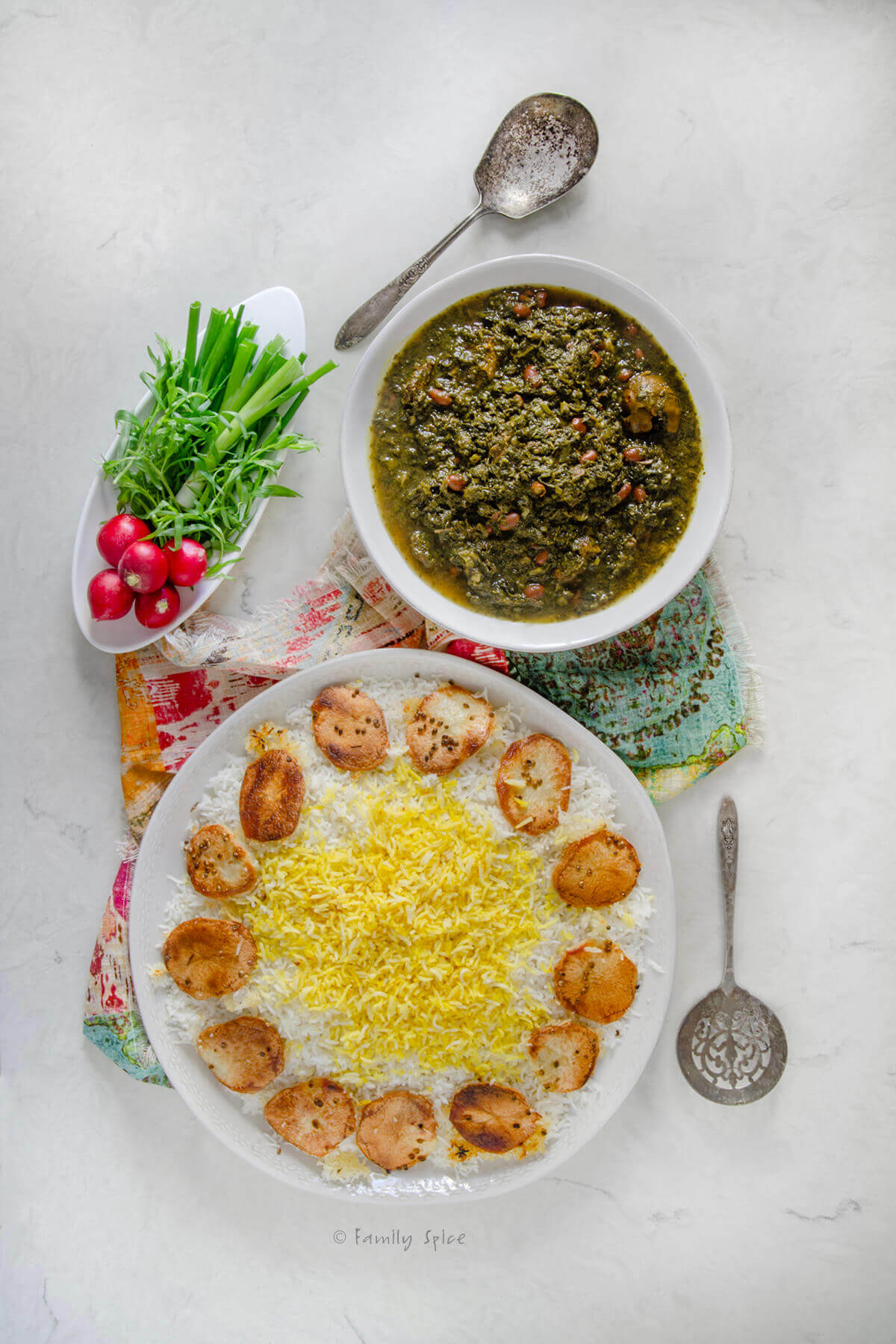 Top view of Persian rice on a platter, ghormeh sabzi in a bowl and fresh radishes and herbs