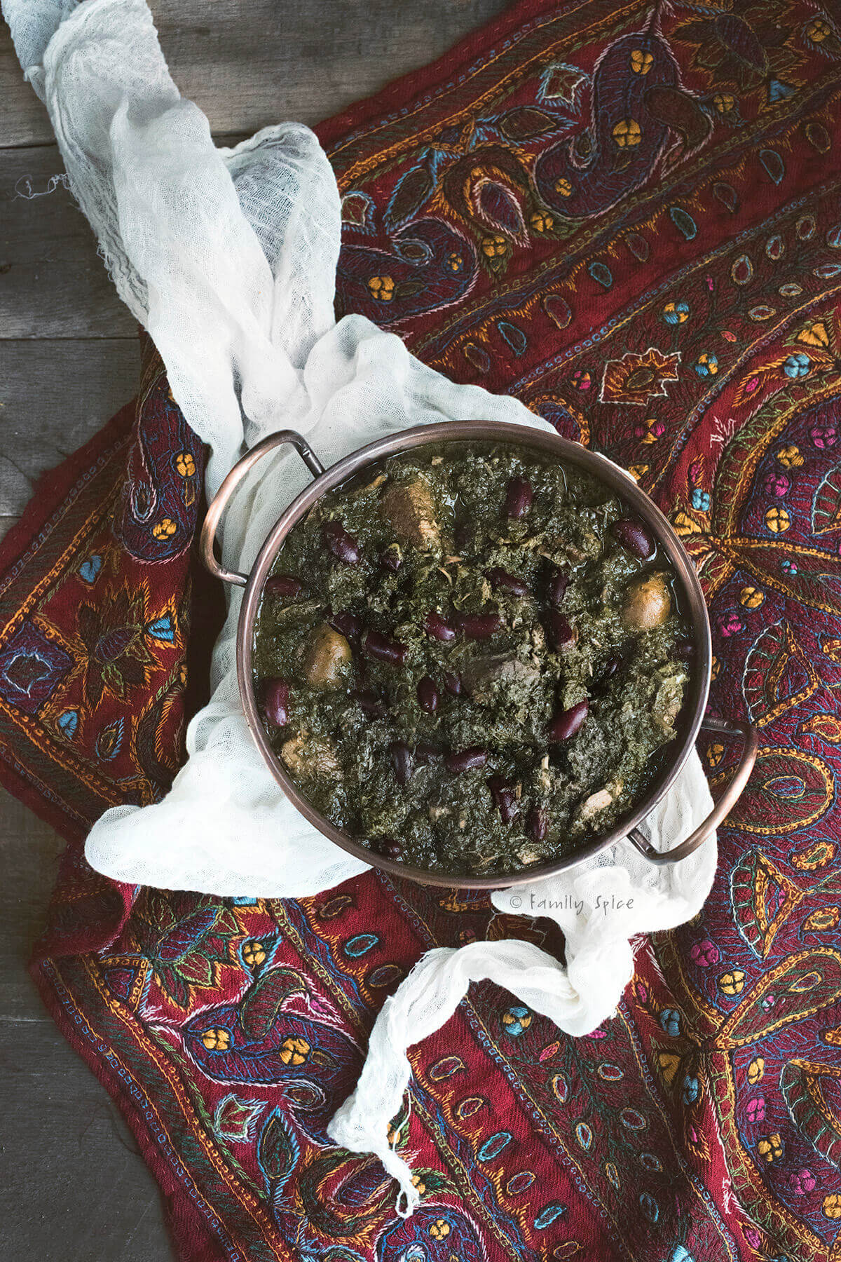 Top view of a copper bowl with ghormeh sabzi (herb stew) on a Persian tapestry