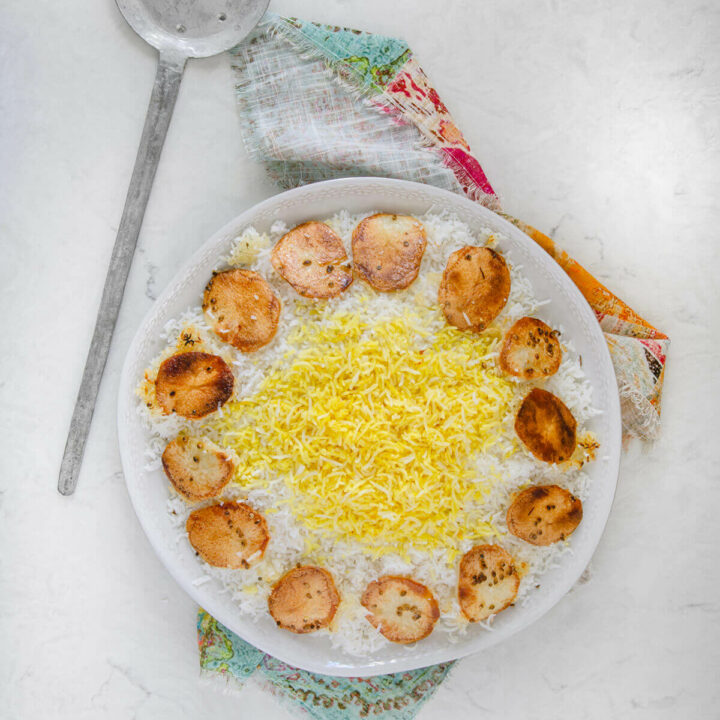 Top view of a round platter with Persian rice topped with saffron rice with potato tahdig around it