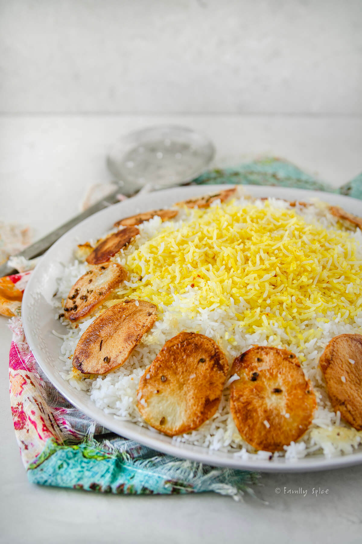 Side view of a platter with Persian rice topped with saffron rice with potato tahdig around it