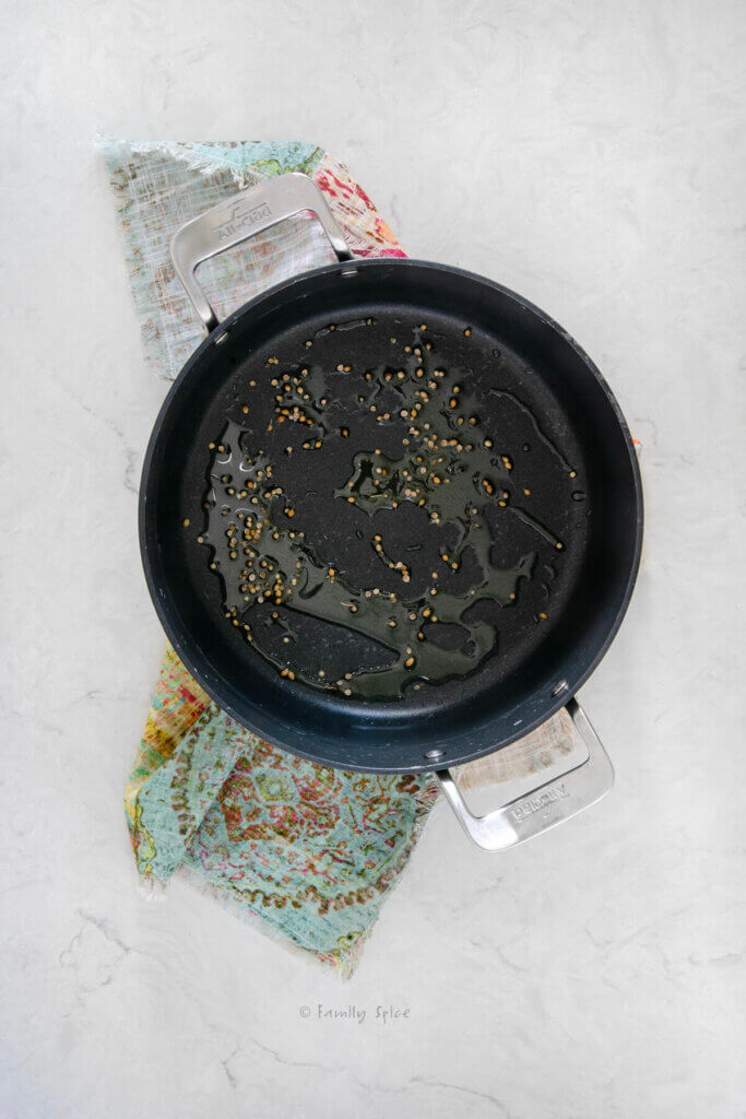 Top view of a non-stick pot with oil and coriander seeds along the bottom