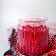 Side view of a glass jar with raspberry compote in it