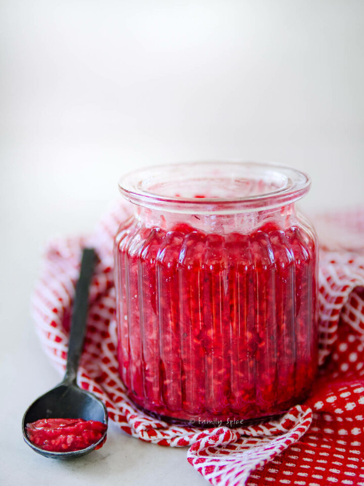 Side view of a glass jar with raspberry compote in it