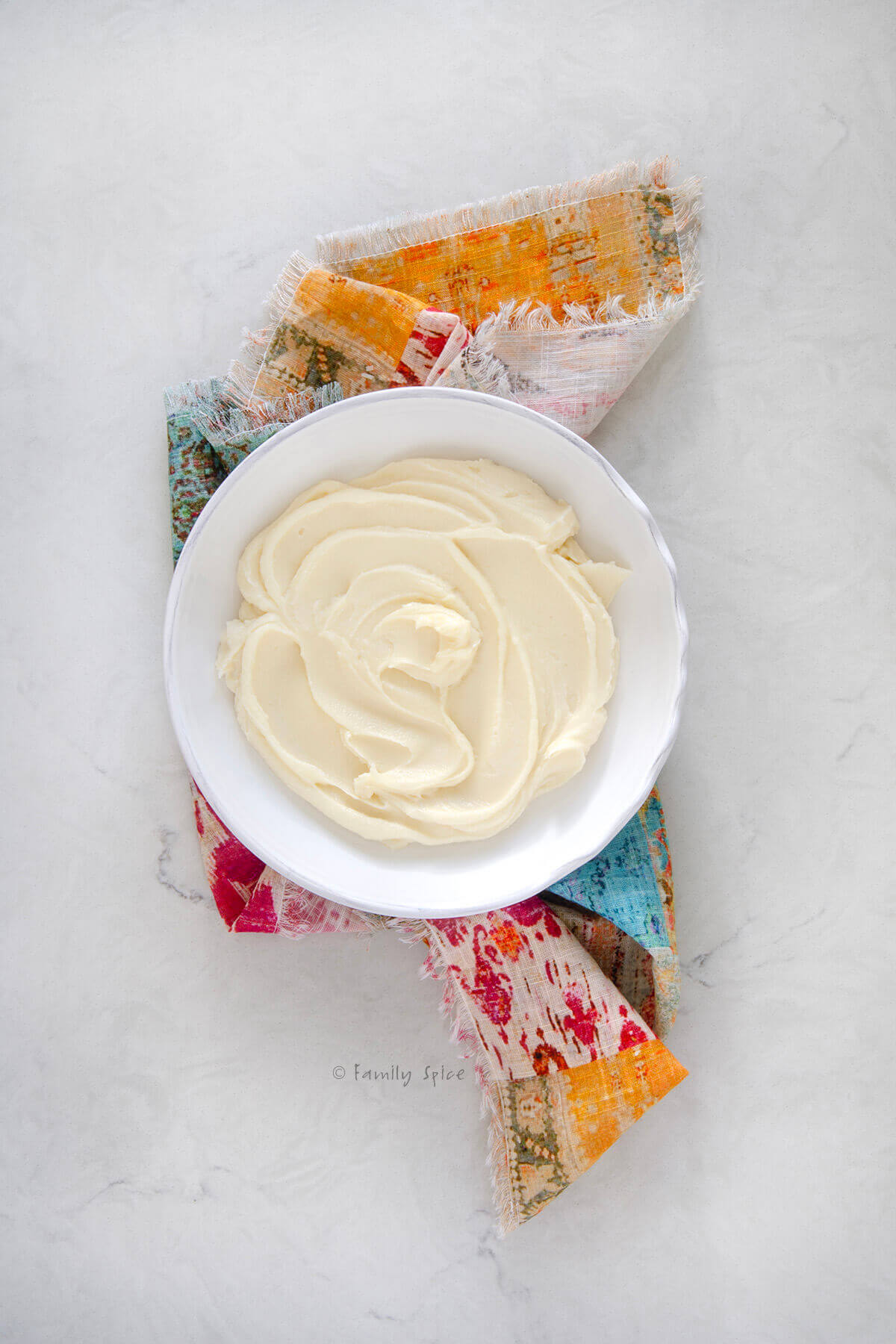 Top view of a white shallow bowl with whipped brie in it on a colorful napkin
