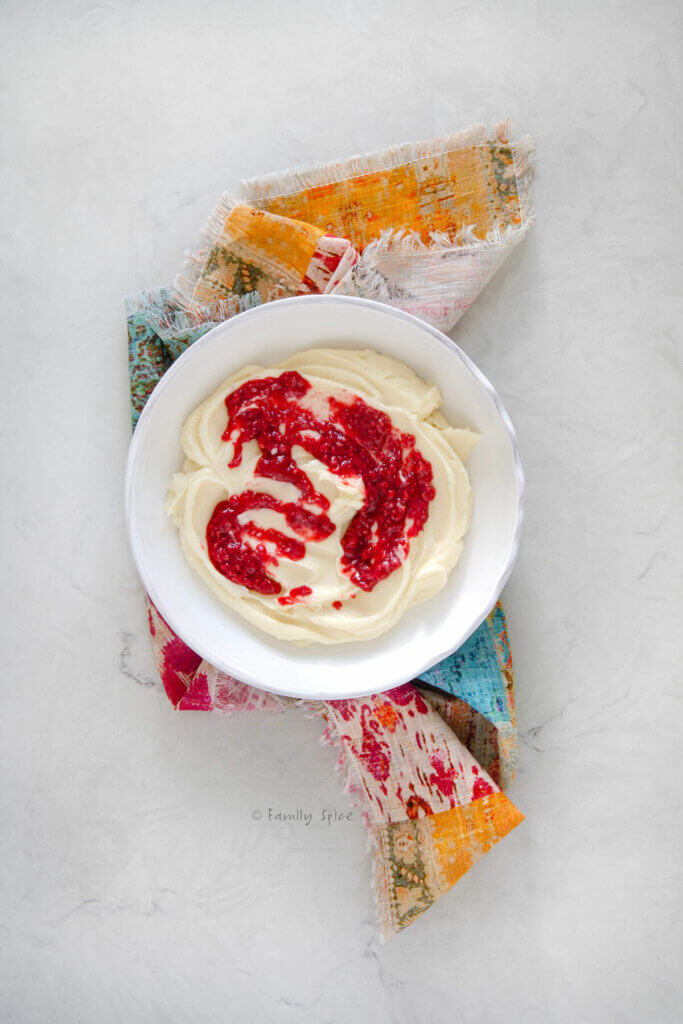 Top view of a white shallow bowl with whipped brie in it, topped with raspberry compote on a colorful napkin