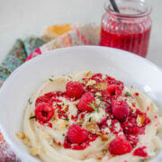 Side view of a white shallow bowl with whipped brie in it, topped with raspberry compote, garnished with bits of crunchy brie bits and rosemary on a colorful napkin